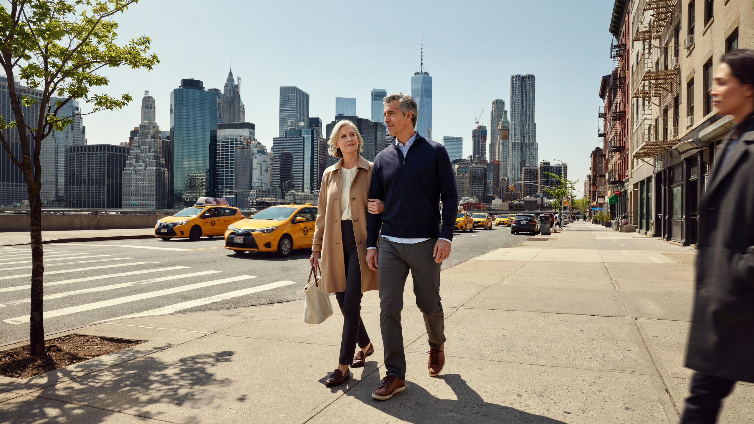 Senior couple walking on New York City sidewalk with Manhattan skyline in background